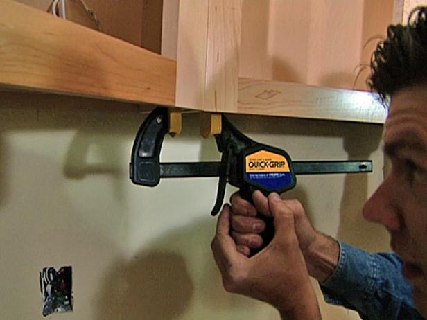 With the second cabinet lifted and held in place, the installers clamp it to the first cabinet using quick-release bar clamps. This will hold it stable while it is being fastened to the wall and corner cabinet.