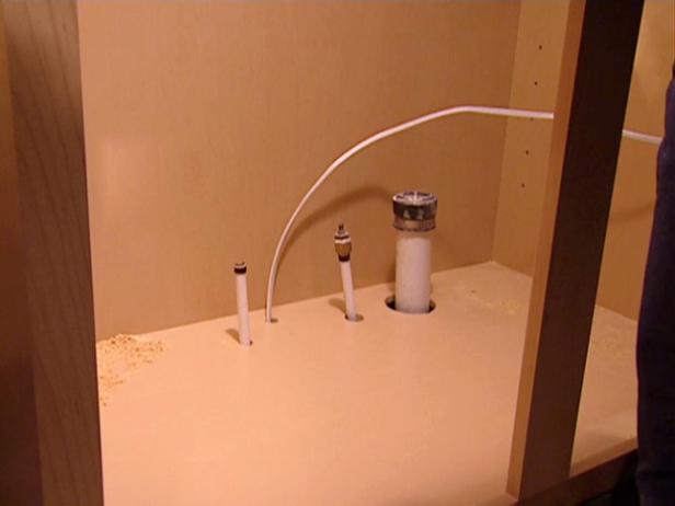 With the holes cut, the sink base cabinet is carefully lowered into position so that the pipes extend up through the holes.