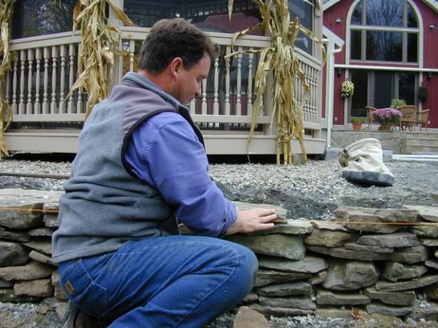 Begin building the wall by setting corner stones (those with a 90-degree corner) at either end of the wall and on both sides of the granite steps. Start setting face stones (those with a flat face) between the corner stones. Every three or four feet, lay a tie-back stone (flat, long and heavy) to provide additional stability. Continue laying corner and face stones to build up the wall until desired height is almost reached. Regularly check that the wall is plumb. For the final course use cap stones.