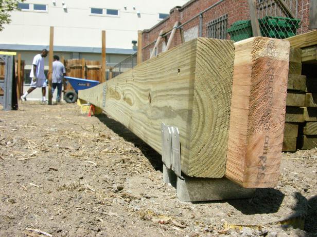 Keeping the more attractive redwood side out, fit the four perimeter boards onto anchor plates set on the caissons. Later, these anchors help permanently tie the deck down.