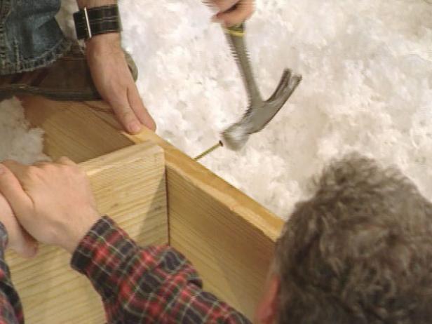 The existing attic floor joists make up the long sides of the opening, but the two shorter headers must be cut and installed. Cut 2x10 boards to fit perpendicularly between the attic floor joists.