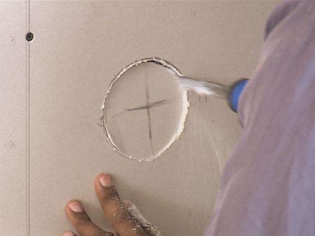 Using a drywall saw, tap the tip of the saw into the drywall paper using a hammer and then cut out any holes needed for vents and outlets.
