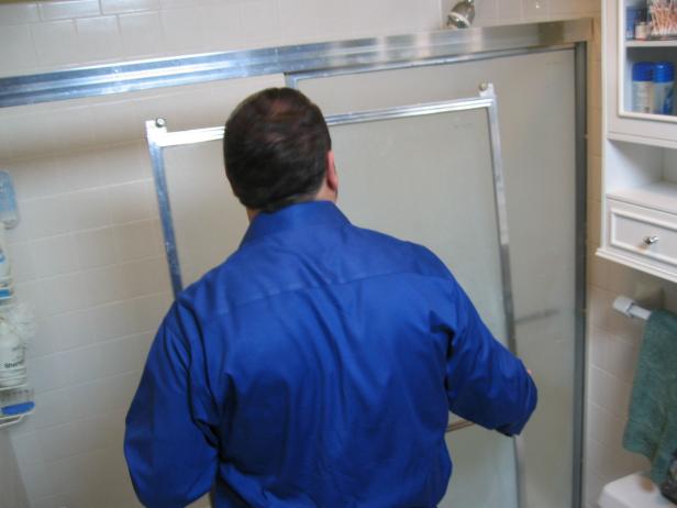 Before you can install the bottom and side jambs of the new tub and shower door, you have to remove the old shower door completely. Lift and remove the outside door panel, then the inside one, followed by the top track.
