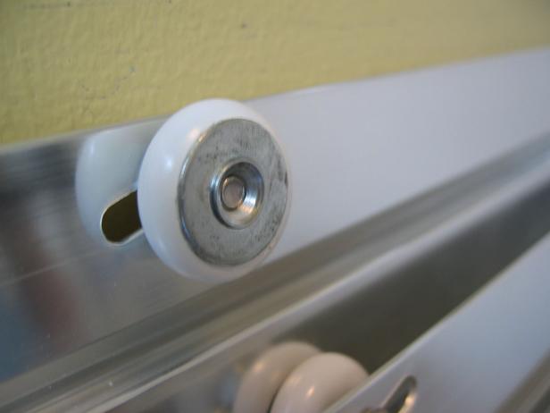 Hanging the doors is a two-step process. Standing on the outside of the tub, lift the inside panel with the rollers facing the shower and hang on the inner rail of the top track. Do the same for the outside panel, where the rollers now face away from the shower and the door will hang on the outer rail of the top track. Push the shower doors to the side, step inside the tub and align the slots on the panel guide with the holes on the bottom track. Insert two pan head screws into the slots and tighten with a screwdriver.