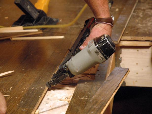 Close up of contractor using a nail gun on a damaged hardwood floor in the disaster house for repair.