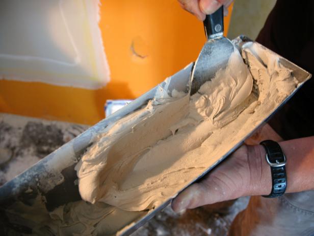 Josh mixes up drywall mud in this container using a scraper to repair damaged wall inside the Disaster House.