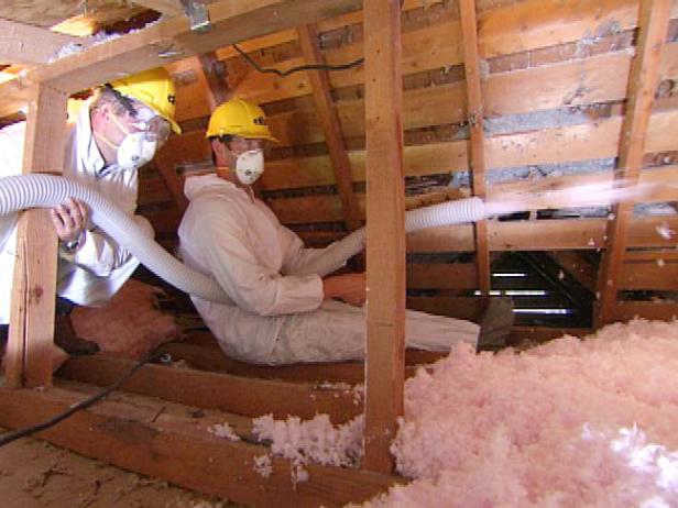 Two men in uniforms spray attic insulation into the space.