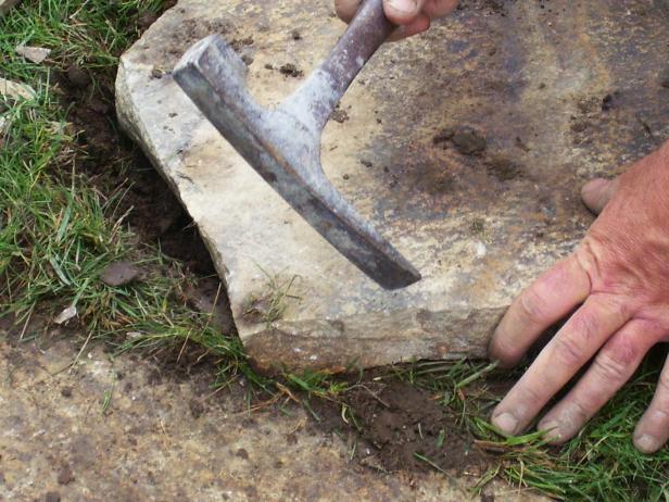 First, use the mason's chipping hammer’s single flat tine to chip or score a cutline across the back of the stone, then turn the stone right-side up and repeat this scoring along a corresponding line across the stone face. Then use the tool’s hammer end to rap sharply along the line to break the stone. Chip away any sharp stone spurs.
