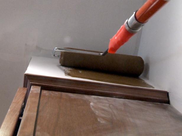 Using a roller brush to paint wall with brown paint.