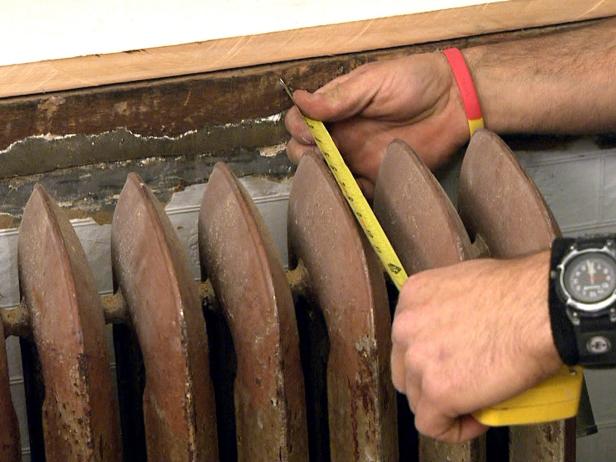 Using a measuring tape to measure the old radiator.