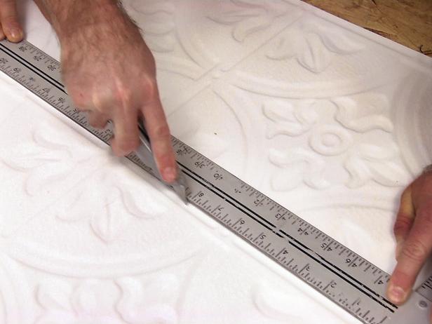 Using a metal straight edge to cut into the tin ceiling panels on this home improvement project.