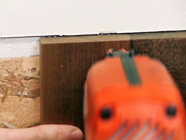 Installing wainscoting wood panels to the wall using a nail gun.