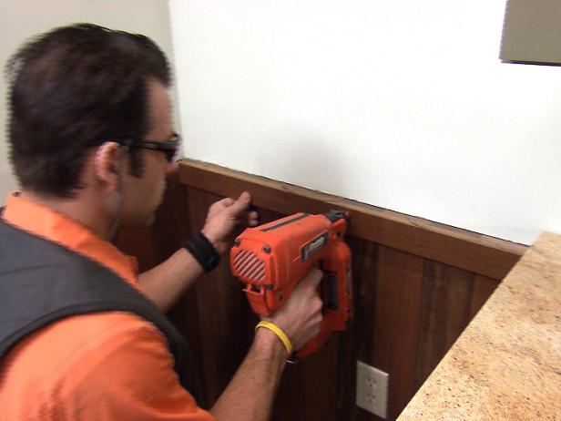 Man uses a nail gun to install an apron around the wainscoting on the wall.