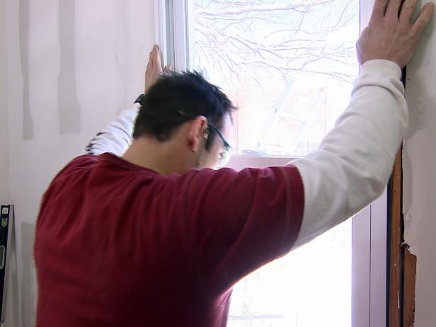Man installs new window in this framed area of this home improvement project.