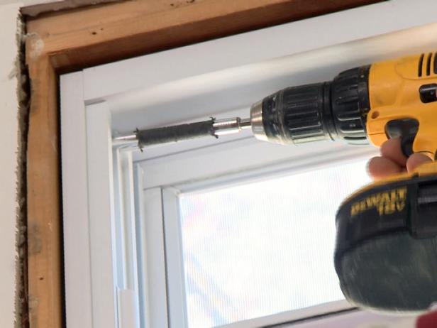 Close up of a drill making a hole for a screw in the side of the window.