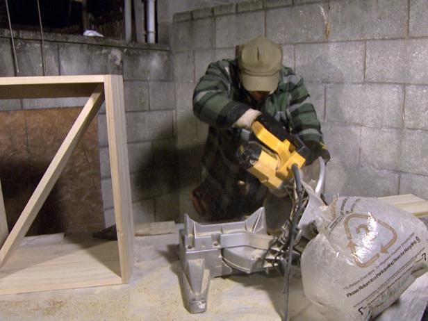 Host uses a saw to cut the wood piece at an angle to make the shelves of the wine rack.