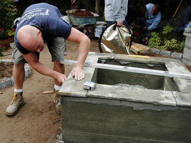 With a sweet design and hard work, this backyard comes to life with a concrete chic fire feature on Yard Crashers. Contractor adds a slate top to the concrete base using a level.