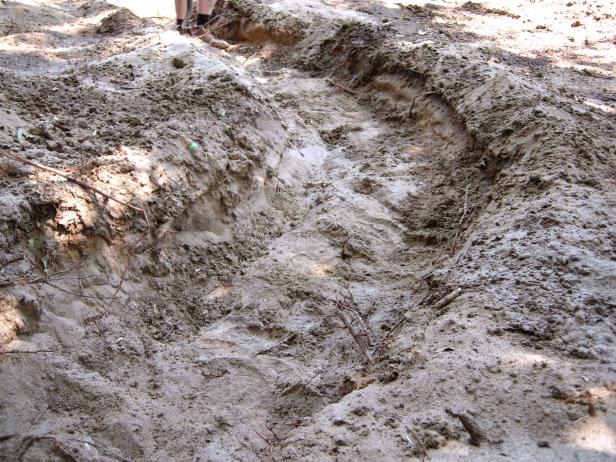 Close up of a dry creek trench area on this episode of Yard Crashers. Contractors dig a trench to help give this back yard a woodsy treat area.