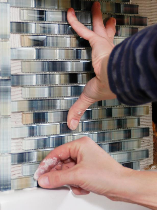 If you are installing sheets of smaller tile with mesh backing ,use a utility knife to cut the sheet to size. Press it firmly with your hands to secure on to wall.