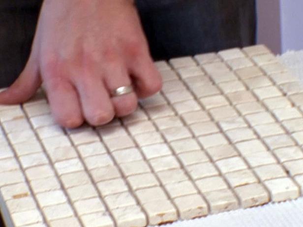Close up of hand pushing down on small tile pieces for installation.