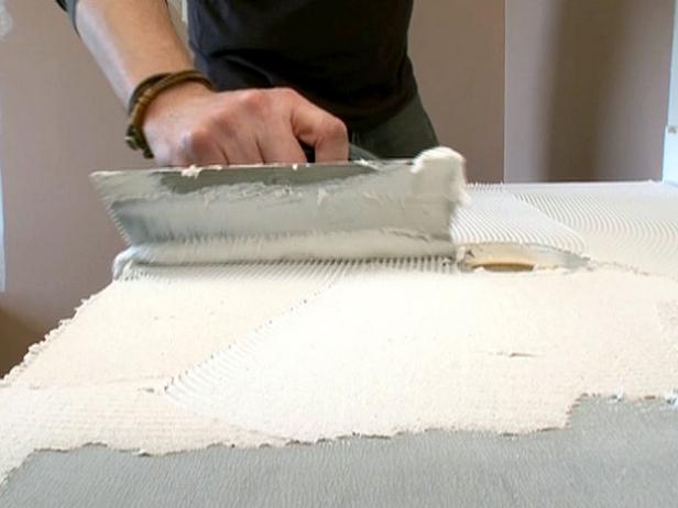 Man uses a trowel to add adhesive to counter for tile install.