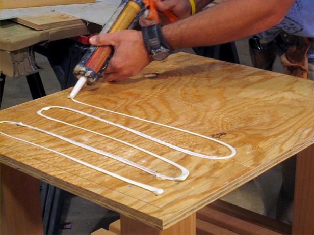 Using a caulking gun to glue wood pieces together to form the kitchen cart furniture project.