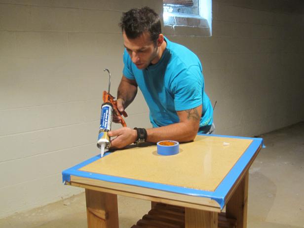 Marc adds silicone to the edges of the wood frame of the kitchen cart construction project.