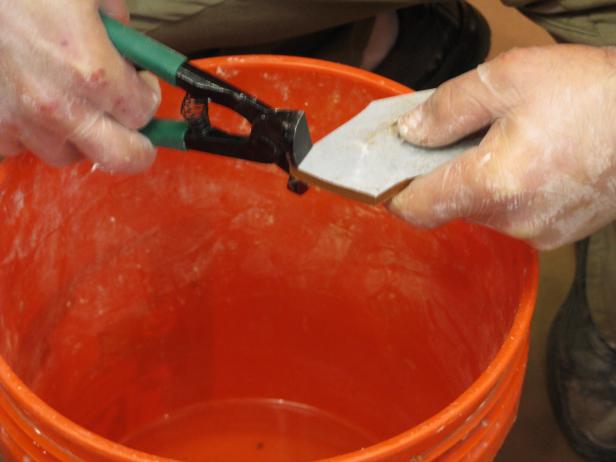 Using a tool to trim tile to shape over an orange bucket.