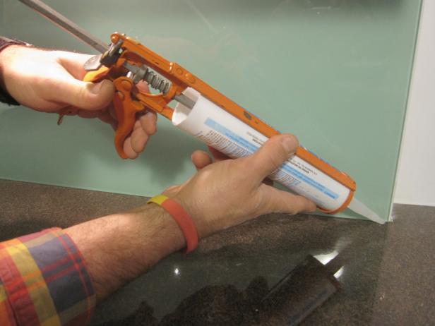 Using a silicone gun to put silicone at the bottom of the glass backsplash