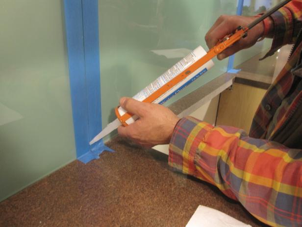 Using a silicone gun to insert silicone into the seams of a glass backsplash