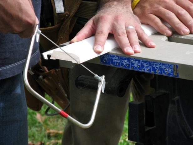 closeup of man using a coping saw to cut the baseboard at the right angle.