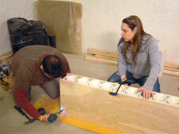 Using a drill to attach the plywood frame to the pvc tubing design for this wine rack construction project.