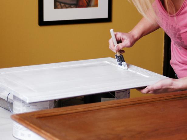Woman paints cabinet with sponge brush using white paint.