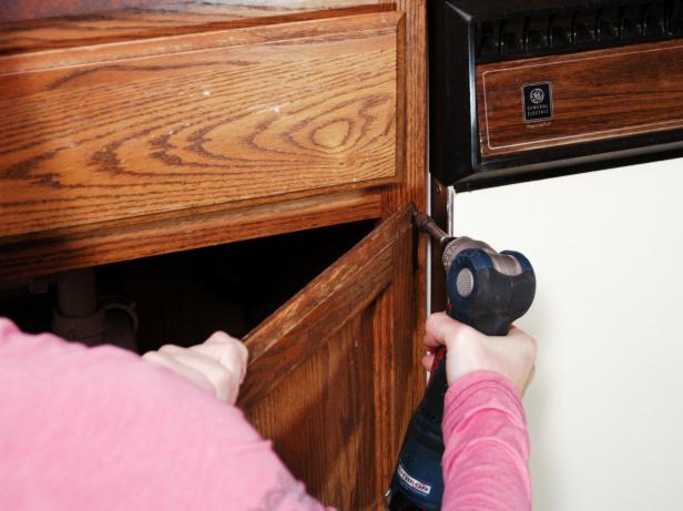 Woman uses a drill to remove the hinges from a cabinet.