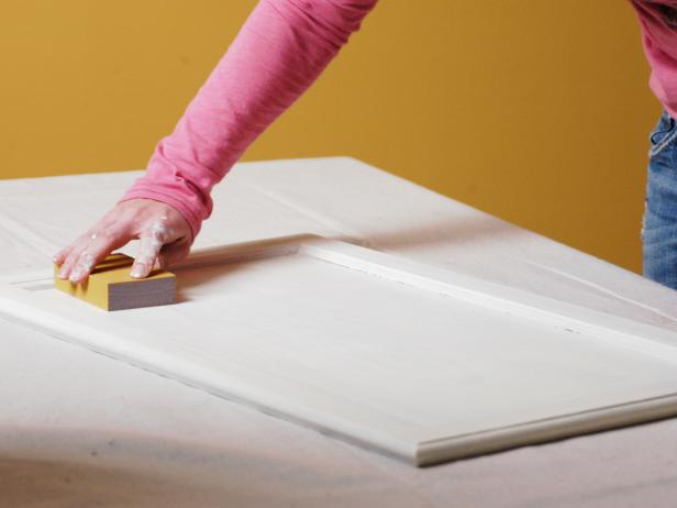 Amy sands the cabinet door between coats of paint.