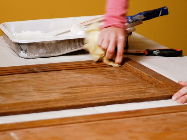 Woman uses a tack cloth to wipe edges of cabinet door.