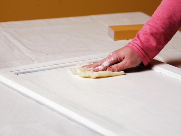 Woman with tack cloth wipes off cabinet door.