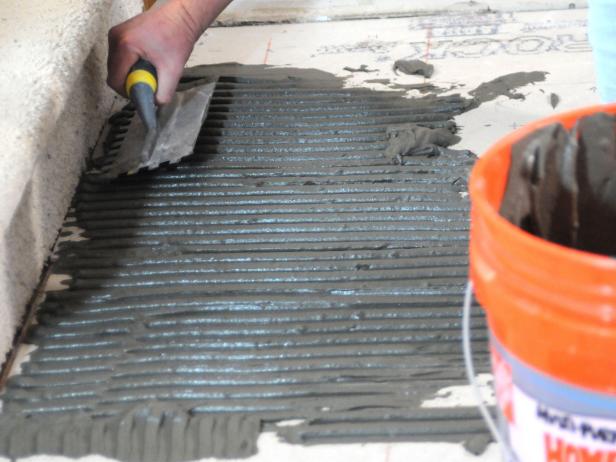 Closeup of Josh spreading thin set on the sub floor using a trowel and bucket.
