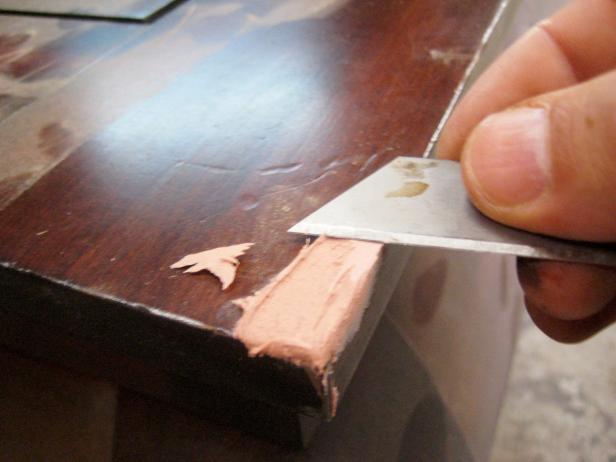 Use a razor blade to score the area so that the filler has some roughness to adhere to. On the damaged section, make several small cuts in the wood in a crisscross pattern.