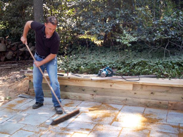 Now that the pavers are set in the base, use a push broom to fill in the joints with a fine layer of sand. Then, sweep off the excess sand from the patio surface.