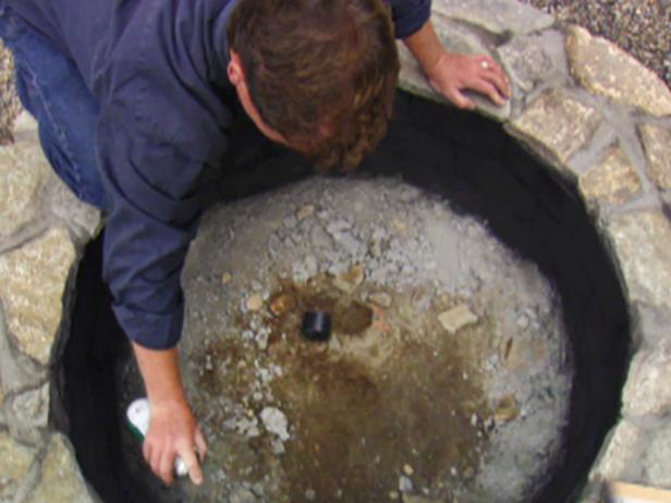 To give the fire bricks on the inside of the structure a uniform finish, spray paint the bricks black using a high-heat stove paint. Fill the pit with a base layer of river rocks.