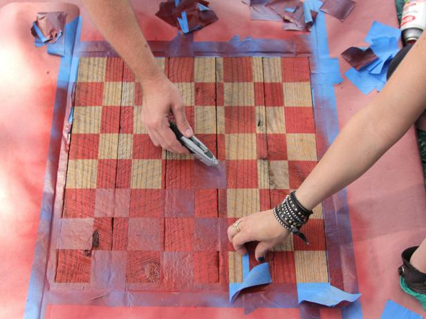 When the taped squares for the board are complete, spray-paint or brush paint the uncovered squares. Allow the surface to dry. Remove the tape to expose the checkerboard pattern on the rough table surface.