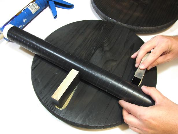 Cut the spacers to width and apply spray paint to the faces and ends. Apply construction adhesive to the bottom edge of the spacers and position them. Use one of the legs as a guide for positioning the spacers to allow for enough room for the legs in the final assembly. Allow the adhesive to cure.