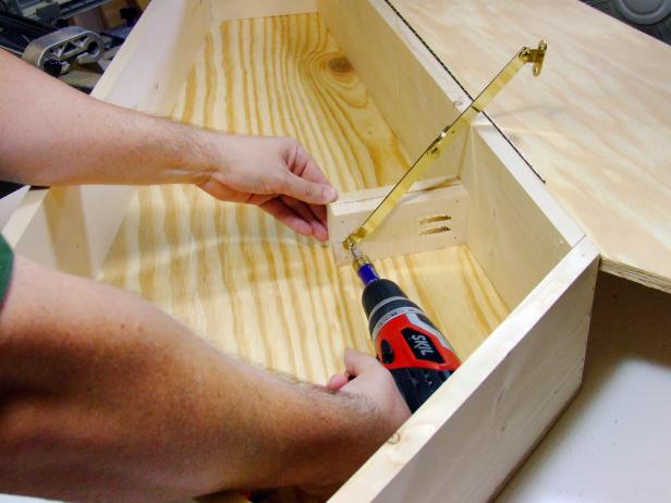 Turn over the coffin assembly. Drill a pilot hole for the folding support hinge centered across the width and 1/2-inches from the end of the support block assembly. Attach the folding support hinge to the support block assembly using one of the screws supplied with hinge.