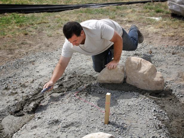 Mix up a small batch of cement mortar and sand, following the instructions on the bag. Fill the bottom of the circular trench with the cement mortar and place the biggest stones in the mix.