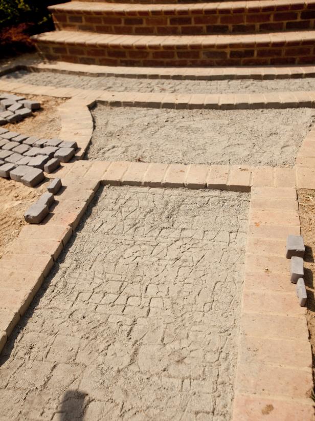 The cobblestones need a layer of stone dust to bed down the stones when pressure is applied. Spread 2” of stone dust on top of the concrete pad and inside the brick border. Level the dust before laying cobblestone.