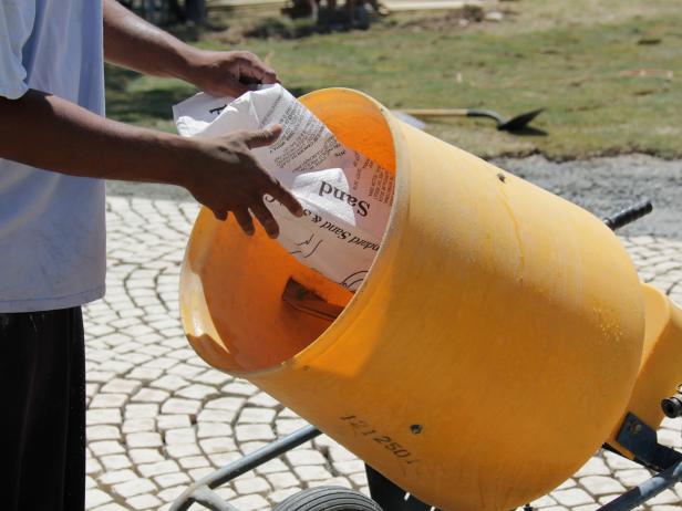 Empty a bag of silica sand into a small, rental mixer.