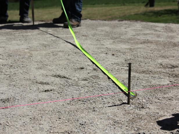 To mark the perimeter, ask a helper to hold a tape measure at the center grade stake and walk in a circular direction at the radius while spraying the sub-base with the marking paint.