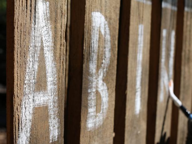 Once the overall design has been painted and has dried, either stencil or free-hand letters or numbers on to the planks.