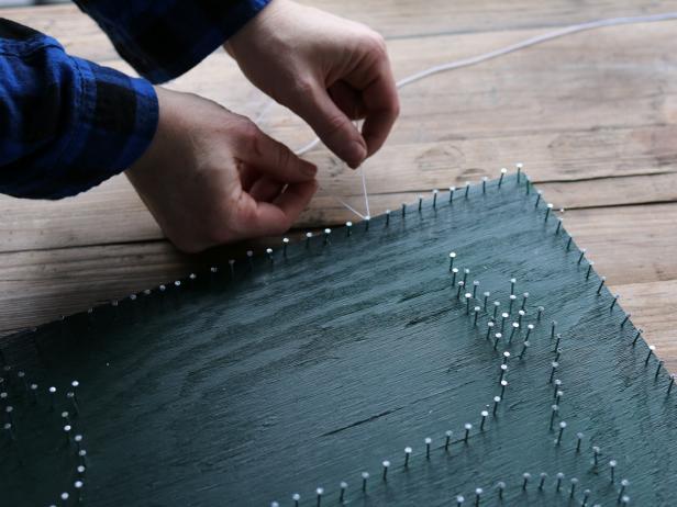 Unfurl spool of white string, then knot it in place along a perimeter nail.